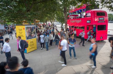 Londra, İngiltere, İngiltere-21 Temmuz 2019: Ziyaretçiler, aralarında pembe bir Londra otobüsünün de yer aldığı yeniliğe bakarak Thames Nehri Embankment 'ı boyunca yürüyorlar.