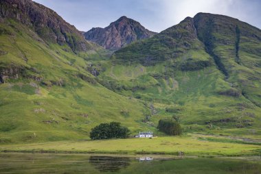 In Lochaber,dwarfed by the majestic mountains along the Valley of Glencoe,the wee picturesque cottage,sits between a clump of trees used by hiking climbers,sitting amongst lush,green summer grass.