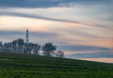 Güzel, nazikçe tarıma elverişli topraklarda, uzaktaki ağaçlardan çıkan, Güney İngiltere 'deki tarım arazilerinde kablolar akan, artçı ışıkla parlayan katmanlı bulutlar..