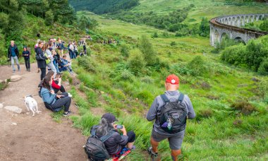 Glenfinnan, Inverness-shire, İskoç Highlands-21 Temmuz 2022: Çocuklar ve yetişkinler bir yamaçta benzer şekilde, Harry Potter filmlerinde yer alarak ünlü olan ikonik buhar lokomotifine dikkat edin.