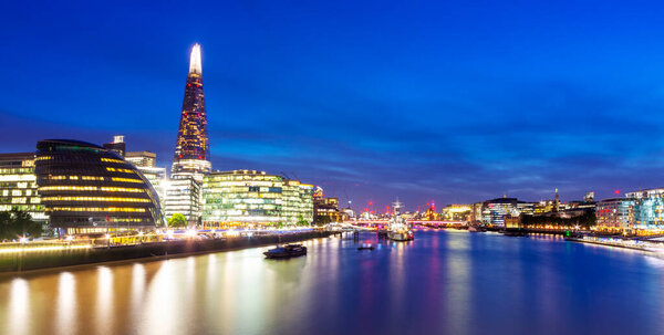 Panoramic view,looking south west,the Shard,HMS Belfast and other buildings along London South Bank, illuminated against inky blue summer sky.