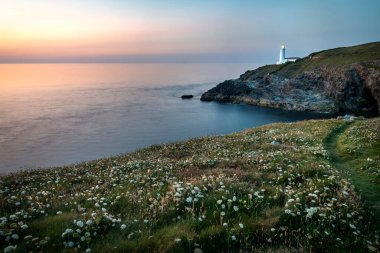 Tarihsel deniz feneri, popüler bir turistik yer, Kuzey Cornish 'in önde gelen bir simgesi, arka planda parlıyor, sakin yaz havasında, yaz ortasında, gün batımından sonra, gemileri uyarıyor..