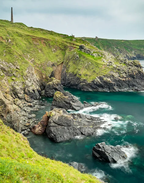 夏天平静的蓝色绿色大西洋 在悬崖顶上的锡矿烟囱和被毁的采矿建筑 在悬崖下面锯齿状的岩石上的阳光 — 图库照片