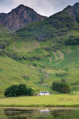 In Lochaber,dwarfed by the majestic mountains along the Valley of Glencoe,the wee picturesque cottage,sits between a clump of trees used by hiking climbers,sitting amongst lush,green summer grass.
