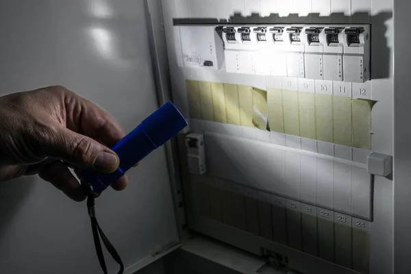 德国一名男子在停电时用蓝色手电筒照明 在配电箱内装有保险丝的保险盒 免版税图库照片