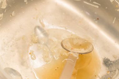 Almanya 'da mutfak lavabosunda salata sosu sirke yağı ve plastik yemek kaşığıyla kullanılmış kirli salata kasesini kapatın.