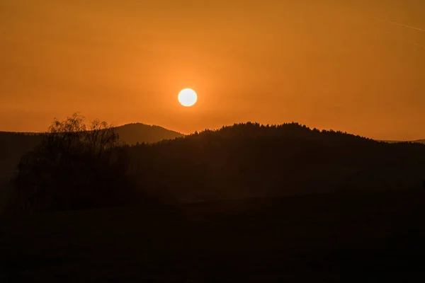 Close up of sun during sunset over horizon with mountain hill landscape in foreground, Germany