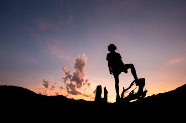 Dağların gölgeleriyle çevrili bir kütüğün üzerindeki genç bir çocuğun silueti. Akşamları yere düşüyor. Egzersiz sonrası dinlenme hissi..