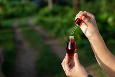 Asyalı kadının el altyapısında seçici odak kırmızı yüz serumu şişesi var. Metin için yer var..