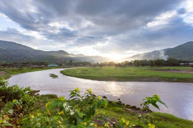 Manzara, nehir kıvrılır, dağlar, gökyüzü, gün batımı sıcaklık ve tazelik hissi verir. Doğal arka plan tasarımı için yeşil çayır hayvancılık alanı Tayland Hayvan Çiftliği