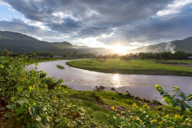 Manzara, nehir kıvrılır, dağlar, gökyüzü, gün batımı sıcaklık ve tazelik hissi verir. Doğal arka plan tasarımı için yeşil çayır hayvancılık alanı Tayland Hayvan Çiftliği