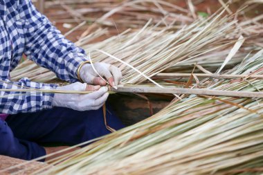 Seçici odaklanma. Büyükannenin eli Tayland 'da kırsal bir köyde saman çatılı doğal ev çatısı inşa ediyor.