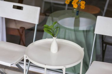 Bir kahve dükkanının önündeki beyaz demire yerleştirilmiş bitkilerin olduğu seçici beyaz vazo. Dükkanda kimse oturmuyor. Görüntü metin için yer var..