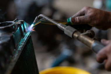 Bir araba tamircisi radyatörü tamir ediyor kurşun maşayla ve radyatör metalini doldurmak için ateşi kullanıyor. Gaz üfleyici