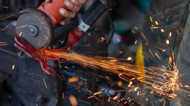 Genç işçiler metal öğütücüleri kullanır. Metal öğütücüden güzel turuncu parıltılar tasarlamak ve modifiye etmek için bir motosikletin çelik parçalarını..