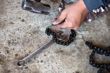 Motosiklet zinciri kesiliyor. Kesmek için kullanılan aletler çivi ve çekiçtir. Motosiklet tamircisinin eline yaklaş..