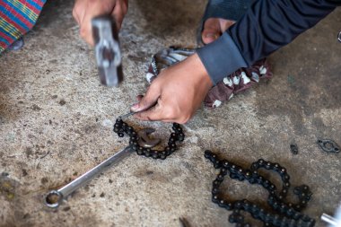 Motosiklet zinciri kesiliyor. Kesmek için kullanılan aletler çivi ve çekiçtir. Motosiklet tamircisinin eline yaklaş..