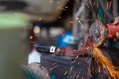 Genç işçiler metal öğütücüleri kullanır. Metal öğütücüden güzel turuncu parıltılar tasarlamak ve modifiye etmek için bir motosikletin çelik parçalarını..