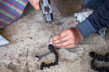 Motosiklet zinciri kesiliyor. Kesmek için kullanılan aletler çivi ve çekiçtir. Motosiklet tamircisinin eline yaklaş..