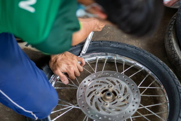 Bir motorsikletin tekerleklerinin yakın plan çekimi, bir tamirci tarafından, sızıntılar nedeniyle, tekerlekleri değiştirmek ve tekrarlamak için kaldırılıyor..