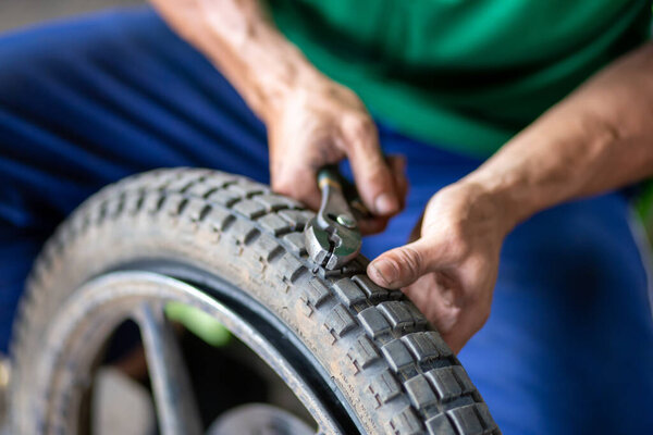 Механик мотоцикла пытается использовать устройство, чтобы извлечь металл из шины, которая вызвала прокол шины.