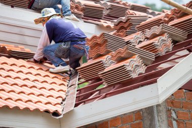 Yeni turuncu çatı kiremitleri, kalın plan, inşaatçılar tarafından çatıda monte ediliyor. Bu çok tehlikeli bir iş. Tayland 'da inşaat işinde çalışan yetenekli teknisyenler tarafından.