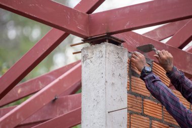 Kırmızı tuğlalar ve duvarcılar binanın duvarlarını örmek için tuğla inşa ediyorlar. Çalışmak profesyonel beceriler gerektirir. Havan ve düzleştirilmiş tuğlaların dengeli bir karışımı.