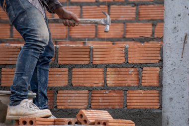 Kırmızı tuğlalar ve duvarcılar binanın duvarlarını örmek için tuğla inşa ediyorlar. Çalışmak profesyonel beceriler gerektirir. Havan ve düzleştirilmiş tuğlaların dengeli bir karışımı.