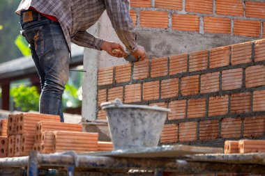 Kırmızı tuğlalar ve duvarcılar binanın duvarlarını örmek için tuğla inşa ediyorlar. Çalışmak profesyonel beceriler gerektirir. Havan ve düzleştirilmiş tuğlaların dengeli bir karışımı.