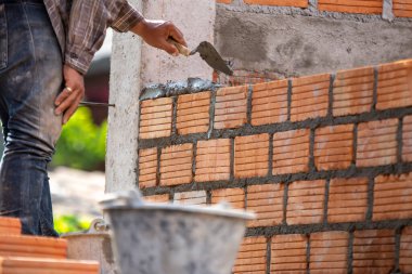 Kırmızı tuğlalar ve duvarcılar binanın duvarlarını örmek için tuğla inşa ediyorlar. Çalışmak profesyonel beceriler gerektirir. Havan ve düzleştirilmiş tuğlaların dengeli bir karışımı.