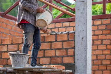 Kırmızı tuğlalar ve duvarcılar binanın duvarlarını örmek için tuğla inşa ediyorlar. Çalışmak profesyonel beceriler gerektirir. Havan ve düzleştirilmiş tuğlaların dengeli bir karışımı.