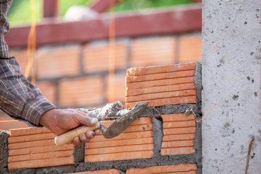 Kırmızı tuğlalar ve duvarcılar binanın duvarlarını örmek için tuğla inşa ediyorlar. Çalışmak profesyonel beceriler gerektirir. Havan ve düzleştirilmiş tuğlaların dengeli bir karışımı.