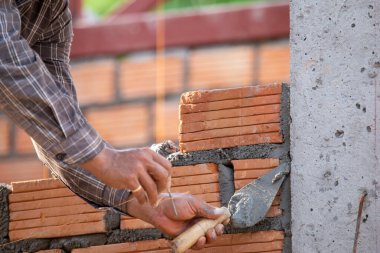 Kırmızı tuğlalar ve duvarcılar binanın duvarlarını örmek için tuğla inşa ediyorlar. Çalışmak profesyonel beceriler gerektirir. Havan ve düzleştirilmiş tuğlaların dengeli bir karışımı.