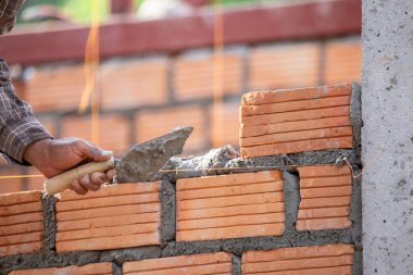 Kırmızı tuğlalar ve duvarcılar binanın duvarlarını örmek için tuğla inşa ediyorlar. Çalışmak profesyonel beceriler gerektirir. Havan ve düzleştirilmiş tuğlaların dengeli bir karışımı.