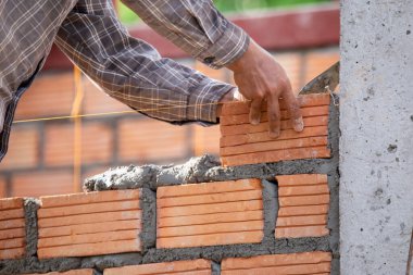 Kırmızı tuğlalar ve duvarcılar binanın duvarlarını örmek için tuğla inşa ediyorlar. Çalışmak profesyonel beceriler gerektirir. Havan ve düzleştirilmiş tuğlaların dengeli bir karışımı.