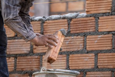 Kırmızı tuğlalar ve duvarcılar binanın duvarlarını örmek için tuğla inşa ediyorlar. Çalışmak profesyonel beceriler gerektirir. Havan ve düzleştirilmiş tuğlaların dengeli bir karışımı.