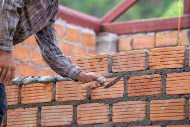 Kırmızı tuğlalar ve duvarcılar binanın duvarlarını örmek için tuğla inşa ediyorlar. Çalışmak profesyonel beceriler gerektirir. Havan ve düzleştirilmiş tuğlaların dengeli bir karışımı.
