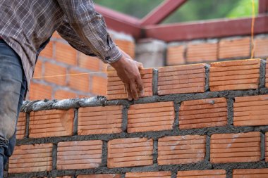Kırmızı tuğlalar ve duvarcılar binanın duvarlarını örmek için tuğla inşa ediyorlar. Çalışmak profesyonel beceriler gerektirir. Havan ve düzleştirilmiş tuğlaların dengeli bir karışımı.