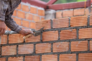 Kırmızı tuğlalar ve duvarcılar binanın duvarlarını örmek için tuğla inşa ediyorlar. Çalışmak profesyonel beceriler gerektirir. Havan ve düzleştirilmiş tuğlaların dengeli bir karışımı.