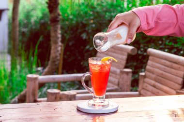 Temiz bir bardaktaki çilek içeceği bir kadın eliyle yoğurtla karıştırılmak üzere..