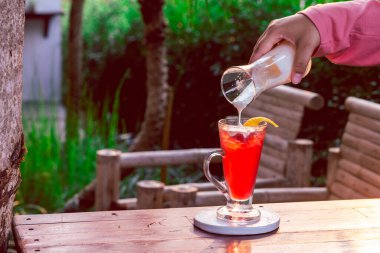 Temiz bir bardaktaki çilek içeceği bir kadın eliyle yoğurtla karıştırılmak üzere..