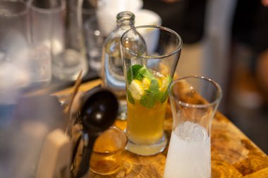 Baristanın bardağa bir şeyler karıştırdığı kafe masasının üzerinde berrak bir bardakta limonlu soğuk bir içecek. Yaz ferahlatıcı içecek