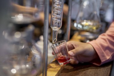 Cam tüp laboratuarının ucunda el ele tutuşan küçük bir bardak. Damıtılmış içecek dükkanı.