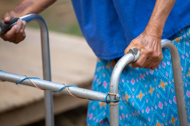 Yürüme iskeleti kullanan yaşlı bir kadın eli, Tayland 'ın kırsal kesimlerinde yaşlı bir büyükanneyle yürüyen bir yardım..