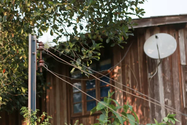 Yakın çekimde çelik direkler, bir elektrik yalıtıcısı ve evin dışındaki eski kablolar, minimalist tasarım güvensiz görünüyor..
