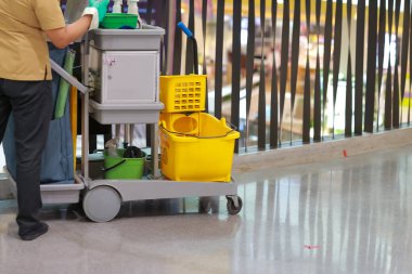 Alışveriş merkezindeki temizlik personeli arabası zemini temizliyor ve içinde bir sürü temizlik malzemesi var..