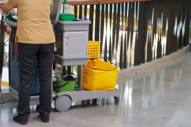 Alışveriş merkezindeki temizlik personeli arabası zemini temizliyor ve içinde bir sürü temizlik malzemesi var..