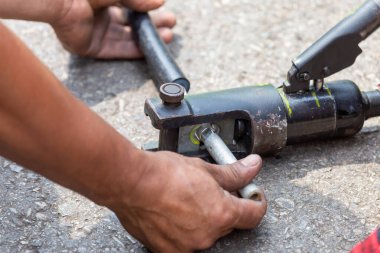 Elektrikçilerin ekipmanlarına yakın çekim yaparak metal kabloları metal bir boruyla birbirine bağlamak için, elektrik yalıtımı kırık kabloya büyük bir klemp kullanılarak takılır..