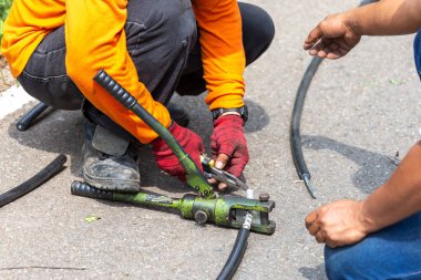 Elektrikçilerin ekipmanlarına yakın çekim yaparak metal kabloları metal bir boruyla birbirine bağlamak için, elektrik yalıtımı kırık kabloya büyük bir klemp kullanılarak takılır..