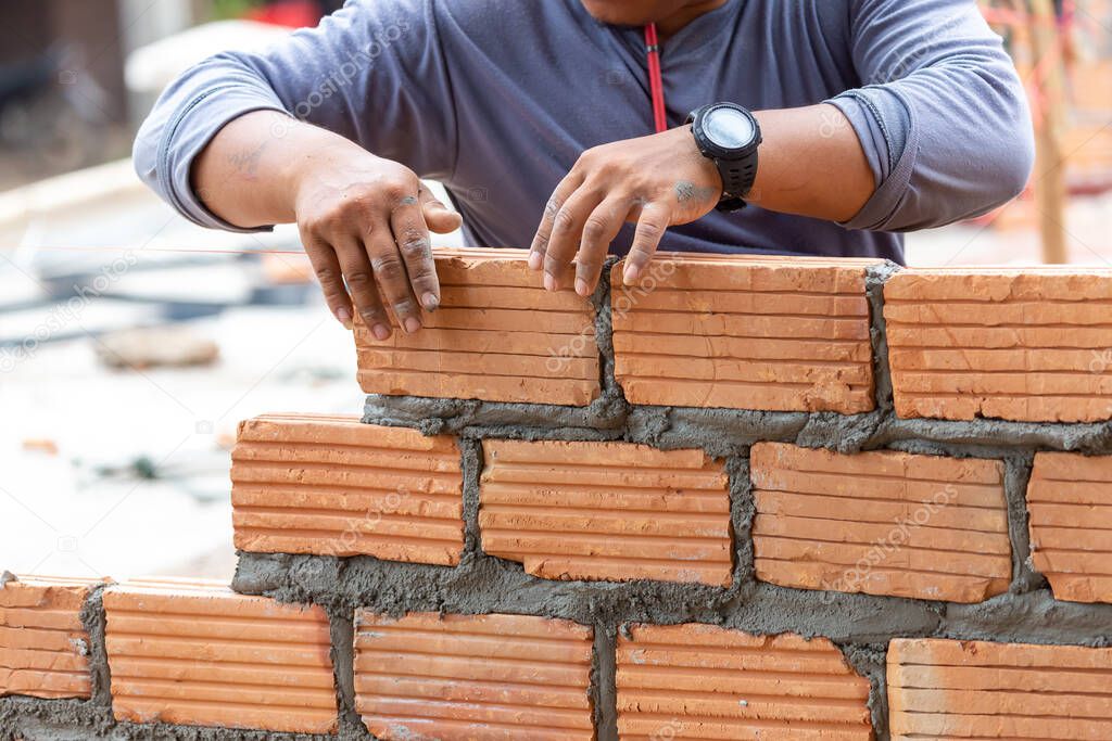 A close up of orange bricks with the hands of a mason We are building the walls of the house, designing the arrangement of bricks to create the walls
